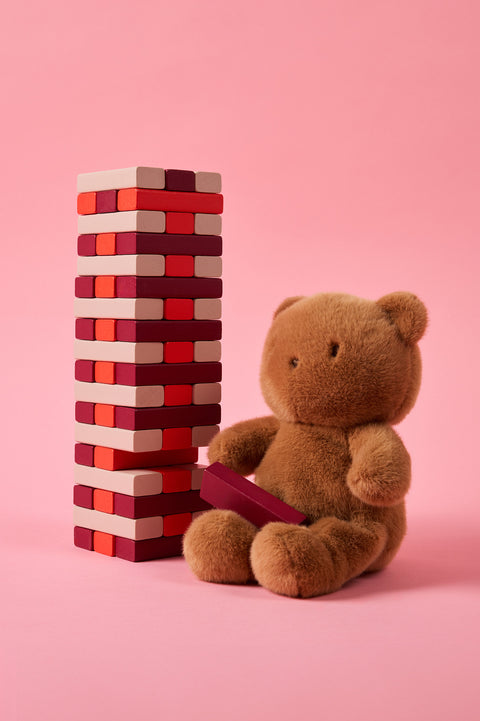 Brown Bobo bear next to a stack of red and beige jenga blocks on a pink background